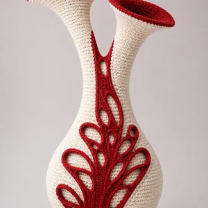 May include: A dual-necked vase crafted from cream-colored yarn with a dense crochet texture. The piece features a prominent, intricate red yarn overlay that forms a branching, leaf-like pattern extending from the base up to the two flared rims.