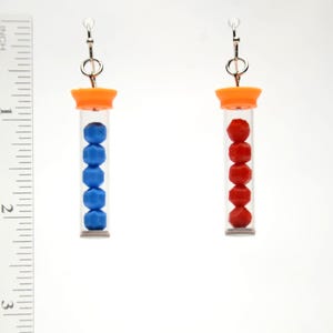 May include: A pair of earrings featuring clear tubes with orange caps and silver-tone hooks. One earring contains five blue beads, and the other has five red beads. The earrings are approximately 1 inch in length.