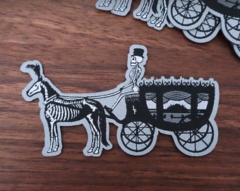 May include: A black and gray patch featuring a skeleton driving a horse-drawn carriage. The horse and driver are depicted as skeletons. The carriage has ornate details. The patch is on a wooden surface. The text "BlackWillow" is at the bottom left.