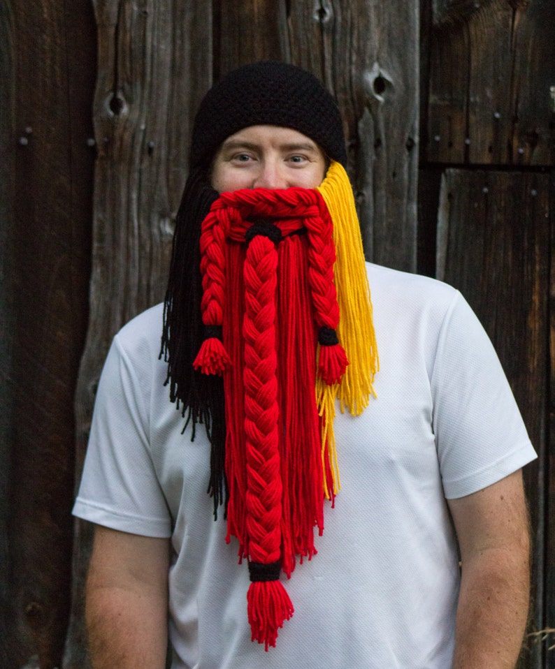 May include: A person wearing a black knit hat with a long, braided yarn beard in black, red, and yellow.