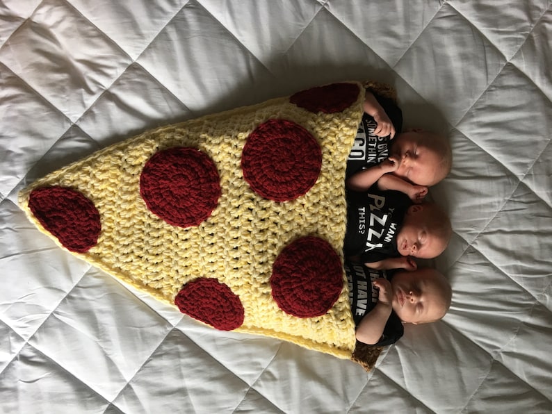 Puede incluir: Tres beb&eacute;s est&aacute;n acostados en una manta de pizza en forma de rebanada de crochet. La manta es amarilla con c&iacute;rculos de pepperoni rojos. Los beb&eacute;s llevan camisas negras con texto blanco que dice "Tengo esta pizza" y "Soy pizza esto?"