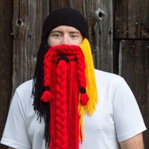 May include: A person wearing a black knit hat with a braided yarn beard in black, red, and yellow.