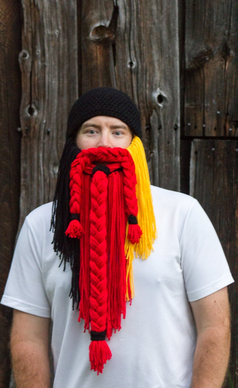 May include: A person wearing a black knit hat with a braided yarn beard in black, red, and yellow.