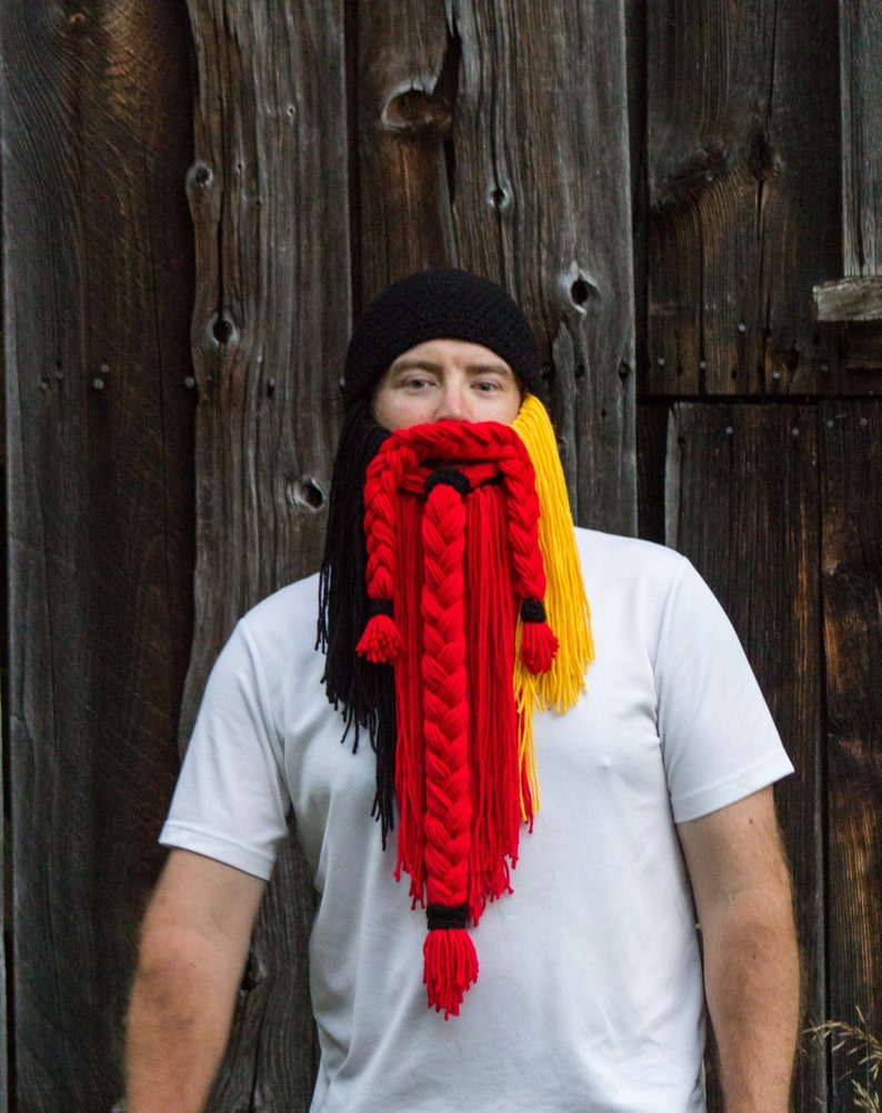 May include: A person wearing a black knit hat with a long, braided yarn beard in black, red, and yellow.