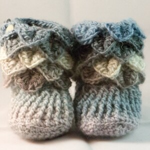 May include: A pair of crocheted baby booties in shades of blue, gray, and white. The booties have a scalloped edge and a textured knit pattern.