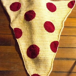 Puede incluir: Una manta de pizza de ganchillo con acentos de pepperoni rojos. Un ni&ntilde;o est&aacute; acostado dentro de la manta.