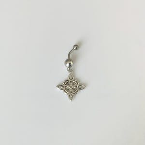 May include: A silver-toned navel ring featuring a curved barbell with a small ball at the top and a larger ball at the bottom. A dangling charm in the shape of a four-pointed Celtic knot with intricate, symmetrical interlaced line patterns.
