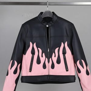 Puede incluir: Chaqueta de cuero negra con diseño de llamas rosas. La chaqueta tiene cuello alzado, cremallera frontal y dos bolsillos con cremallera. Las llamas rosas adornan la parte inferior delantera y las mangas.