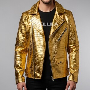 Puede incluir: Chaqueta de cuero dorada y texturizada con un patrón de cocodrilo. La chaqueta tiene un estilo motero clásico con cuello de solapa, cremallera asimétrica y múltiples bolsillos. La chaqueta se lleva sobre una camiseta negra.