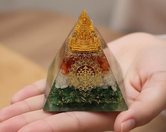 May include: A clear resin pyramid containing layers of green, white, and orange stone chips. A gold-colored Sri Yantra symbol is embedded on the front face, and a small gold-colored temple structure is visible at the apex of the pyramid.