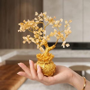 Puede incluir: Una escultura de árbol decorativa con una base dorada en forma de bolsa de dinero con patrones en relieve. Las ramas están hechas de alambre dorado fino adornado con numerosas pequeñas astillas de cristal amarillo translúcido como hojas.