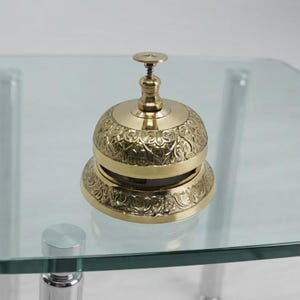 Antique style brass desk bell with engraved pattern and smooth polished surface, elegant decorative accessory for office reception or home decor.