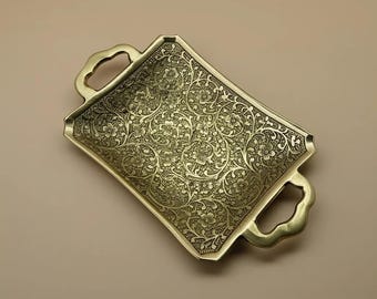 May include: A rectangular brass tray with ornate floral patterns and two curved handles. The tray has a slightly curved shape and a detailed, embossed design. The overall color is a warm, antique gold.