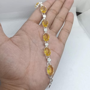 May include: Silver bracelet featuring oval-cut yellow gemstones. The bracelet has a delicate design with small, clear accent stones between the larger gems. The clasp is a simple hook and eye style. The bracelet is shown against a neutral background.