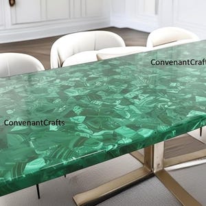 May include: A rectangular dining table with a vibrant green malachite top. The table is supported by a brushed metal base and surrounded by white chairs. The text "ConvenantCrafts" is visible on the table surface.