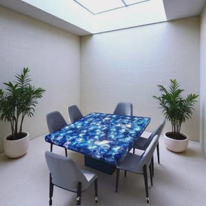 May include: A contemporary dining set with a rectangular table showcasing a blue, agate-style surface. Six grey chairs are arranged around the table. Two potted plants are positioned on either side. The room has white walls and a skylight.