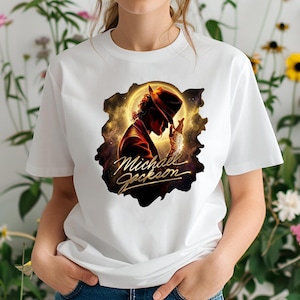 May include: White t-shirt featuring a graphic of Michael Jackson in a hat and suit, set against a golden, cosmic background. The name "Michael Jackson" is written in gold script below the image. The shirt is a classic crew neck.