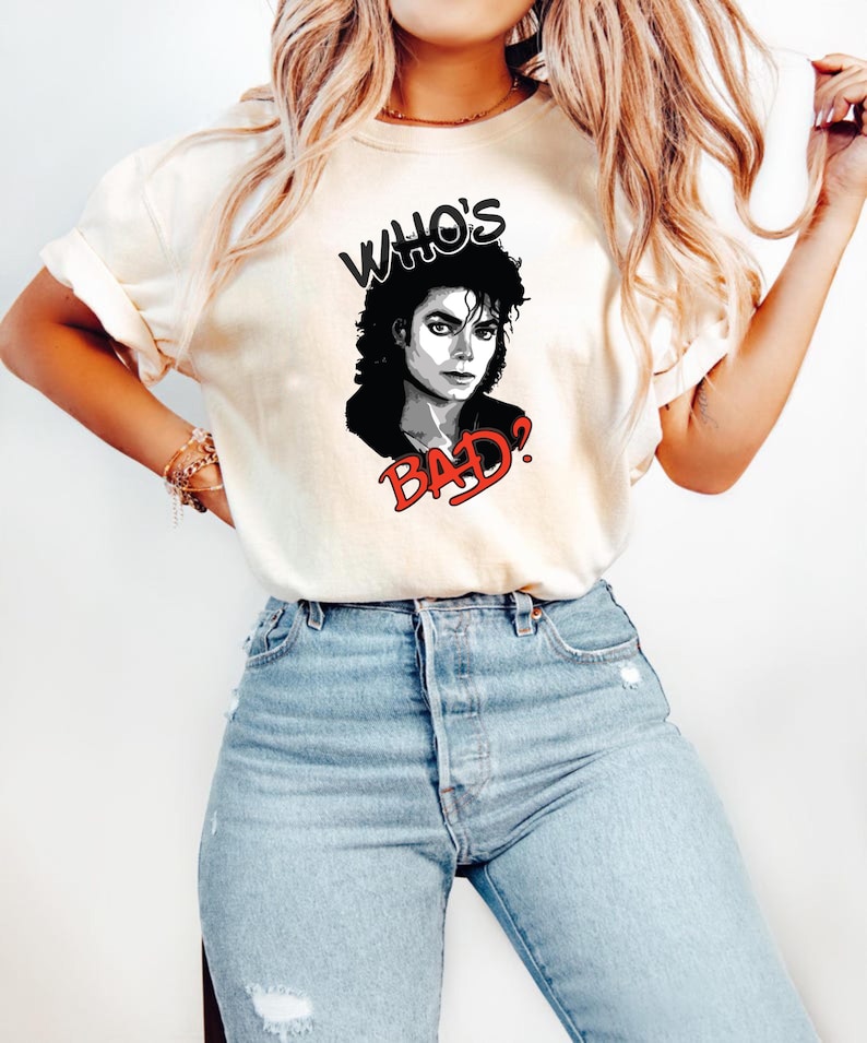 Peut inclure: T-shirt cr&egrave;me avec un graphisme noir et blanc de Michael Jackson et le texte "WHO'S BAD?" en noir et rouge. Le t-shirt est associ&eacute; &agrave; un jean bleu clair.
