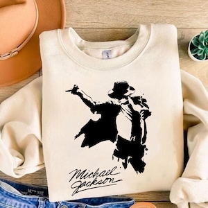 Peut inclure: Sweat-shirt cr&egrave;me avec une silhouette noire de Michael Jackson dans une pose embl&eacute;matique, chapeau et veste. Le nom "Michael Jackson" est &eacute;crit en script stylis&eacute; en dessous. Un v&ecirc;tement d&eacute;contract&eacute; et confortable.