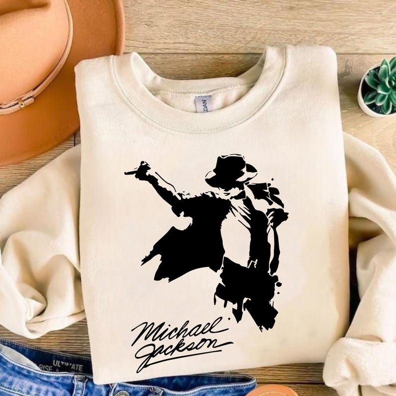 Peut inclure: Sweat-shirt cr&egrave;me avec une silhouette noire de Michael Jackson dans une pose embl&eacute;matique, chapeau et veste. Le nom "Michael Jackson" est &eacute;crit en script stylis&eacute; en dessous. Un v&ecirc;tement d&eacute;contract&eacute; et confortable.