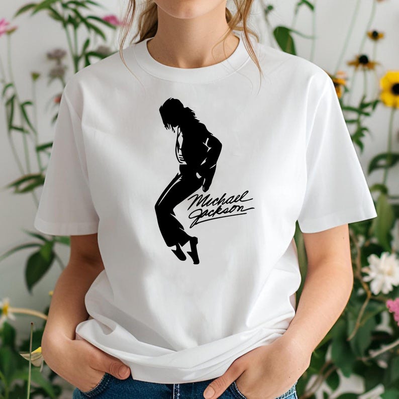Peut inclure: T-shirt blanc avec une silhouette noire de Michael Jackson dans une pose de danse. Le texte en cursive "Michael Jackson" est &eacute;crit en dessous. Le t-shirt est en mati&egrave;re douce et a un col rond.
