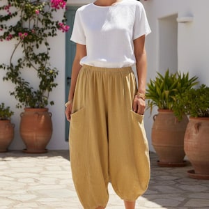 May include: A white short-sleeved crew neck top paired with loose-fitting, mustard-yellow cropped trousers featuring an elastic waistband and two large side pockets. The trousers have a rounded, voluminous silhouette that tapers at the hem.