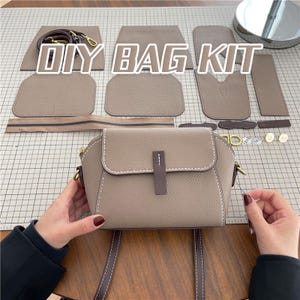 May include: A DIY bag kit with various leather pieces in a neutral beige color, including a completed small crossbody bag. The kit includes a zipper, strap, and hardware. The text "DIY BAG KIT" is displayed in white block letters.