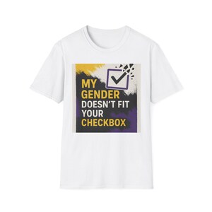 Puede incluir: Camiseta blanca con la frase "MY GENDER DOESN'T FIT YOUR CHECKBOX". El diseño incluye una marca de verificación dentro de un cuadro morado, sobre un fondo de pinceladas amarillas, moradas y negras.