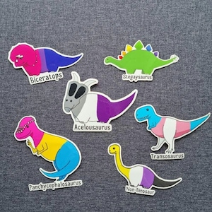 Può includere: Sei adesivi di dinosauri colorati con diverse bandiere arcobaleno. I dinosauri sono un Triceratopo, uno Stegosauro, un Pachycephalosaurus, un dinosauro con un collare, un Tyrannosaurus Rex e un Brachiosaurus. Gli adesivi sono etichettati con i nomi dei dinosauri e la bandiera arcobaleno corrispondente.