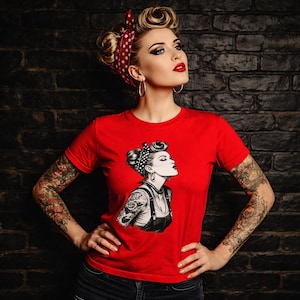 Könnte beinhalten: Ein rotes T-Shirt mit einer Schwarz-Weiß-Illustration einer Frau mit Retro-Frisur und Tätowierungen. Die Frau im Bild trägt ein rotes Polka-Dot-Kopftuch und Creolen. Das T-Shirt ist kurzärmelig.