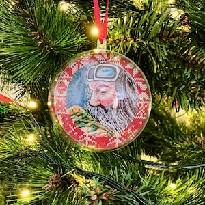 Può includere: Una palla di Natale rotonda e trasparente con un bordo a fantasia rosso e bianco. L'ornamento presenta un'illustrazione ad acquerello di un uomo con una lunga barba bianca e occhiali. Un nastro rosso è attaccato per appenderlo.