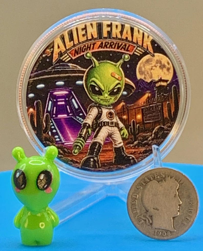 Night Arrival 1 oz copper round standing in its capsule beside a small green alien figurine and a silver coin for size comparison