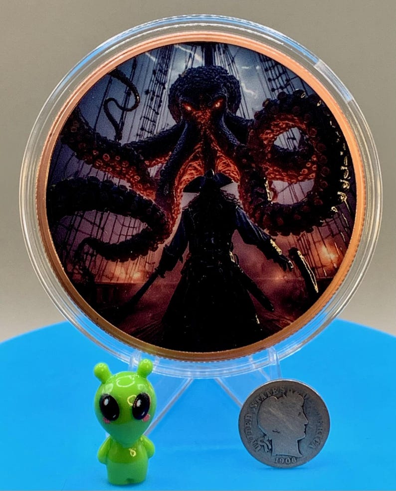 Puede incluir: Una moneda circular de tono cobrizo con una ilustraci&oacute;n colorida de un pulpo oscuro con ojos rojos brillantes sobre una figura pirata en la cubierta de un barco. Una peque&ntilde;a figura de alien&iacute;gena verde y una moneda de diez centavos Barber de 1906.