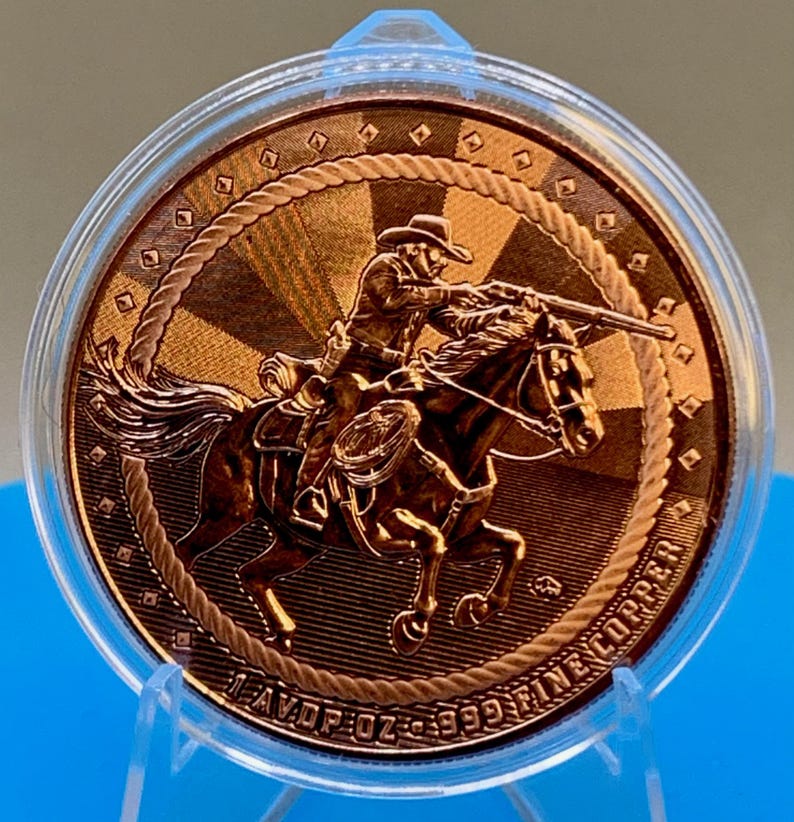 Close-up angled view of the 5 oz .999 fine copper Cowboy round in its protective capsule, showing the raised cowboy-on-horseback design and rope border detail.