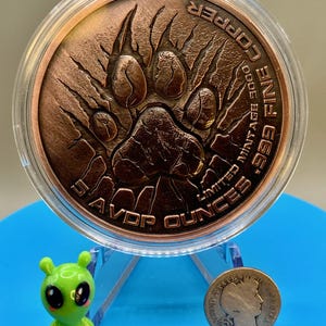 Lion paw print reverse of the copper round on a display stand beside a 1906 Barber dime, showing the round is far larger than a dime