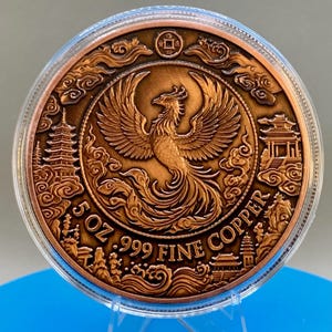 Copper Phoenix round in its capsule with a natural bronze finish, showing a detailed phoenix design surrounded by pagoda towers and the text 5 OZ .999 FINE COPPER.
