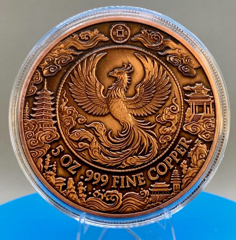 Copper Phoenix round in its capsule with a natural bronze finish, showing a detailed phoenix design surrounded by pagoda towers and the text 5 OZ .999 FINE COPPER.