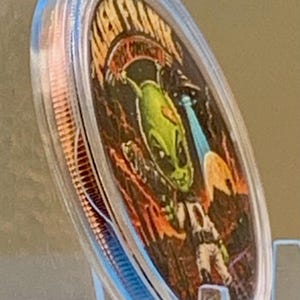 Angled side view of the First Contact 1 oz copper round in its capsule, showing the alien and UFO face and the thick rim of the coin