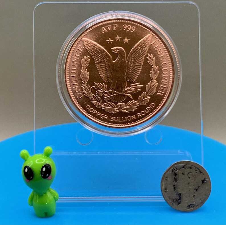 Reverse side of the copper round featuring the eagle-and-wreath "Copper Bullion Round" design, shown with an alien figurine and coin for scale reference