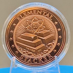 Reverse of the Night Arrival 1 oz copper round in its capsule: "Elemental Stacker" lettering around a stack of copper bars beneath an atom symbol, ringed by stars