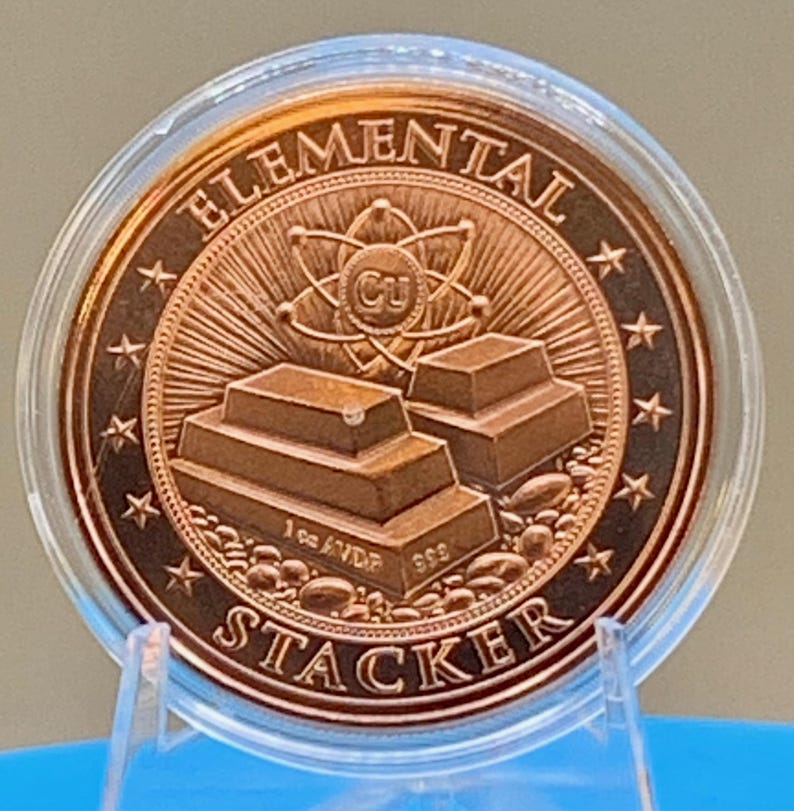 Reverse of the Night Arrival 1 oz copper round in its capsule: "Elemental Stacker" lettering around a stack of copper bars beneath an atom symbol, ringed by stars