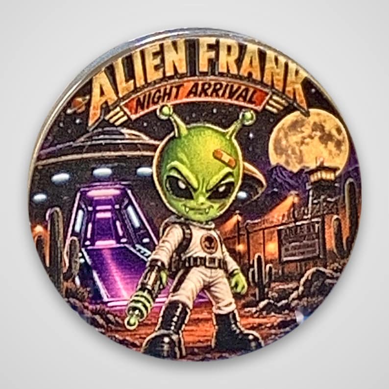 May include: A circular pin featuring a green alien character in a white space suit holding a ray gun. The background shows a desert landscape with a UFO, a full moon, and cacti. The text ALIEN FRANK NIGHT ARRIVAL is printed at the top.