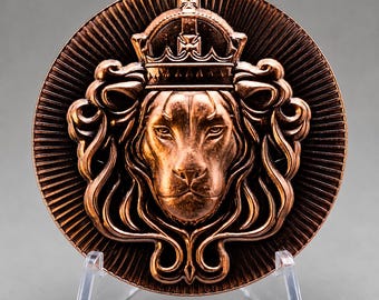 Peut inclure: Un médaillon circulaire de couleur cuivre présentant une sculpture en relief d'une tête de lion portant une couronne. Le lion est centré avec une crinière fluide, entouré d'un motif en rayons de soleil rayonnant vers le bord.