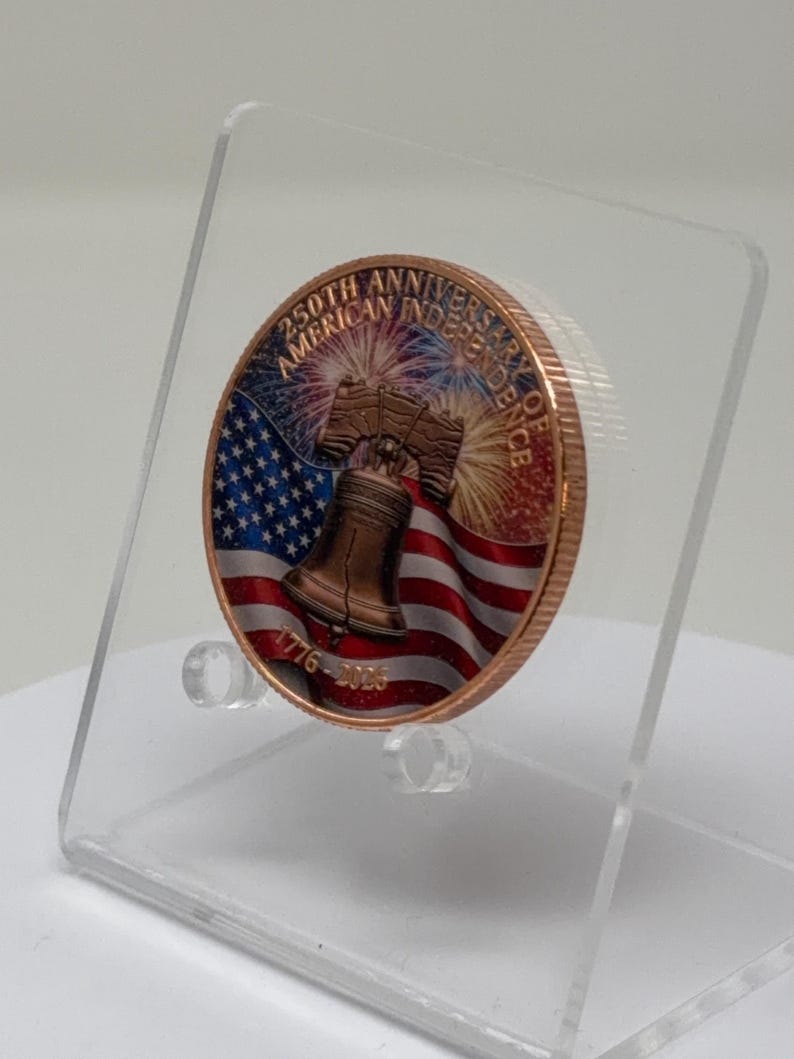 Angled side view of the colorized Liberty Bell and American flag 1 oz copper round on a clear acrylic stand, showing the coin's thickness and raised relief edge