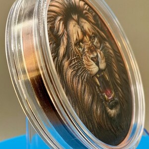 Angled view of the colorized lion obverse in its acrylic capsule, showing the depth of the high relief strike