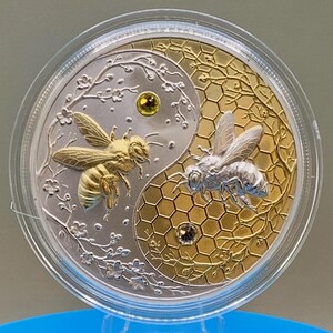 Straight-on view of the Harmony Bee copper round in its capsule, highlighting the raised gold and silver gilded yin-yang bee design and gemstone accents.