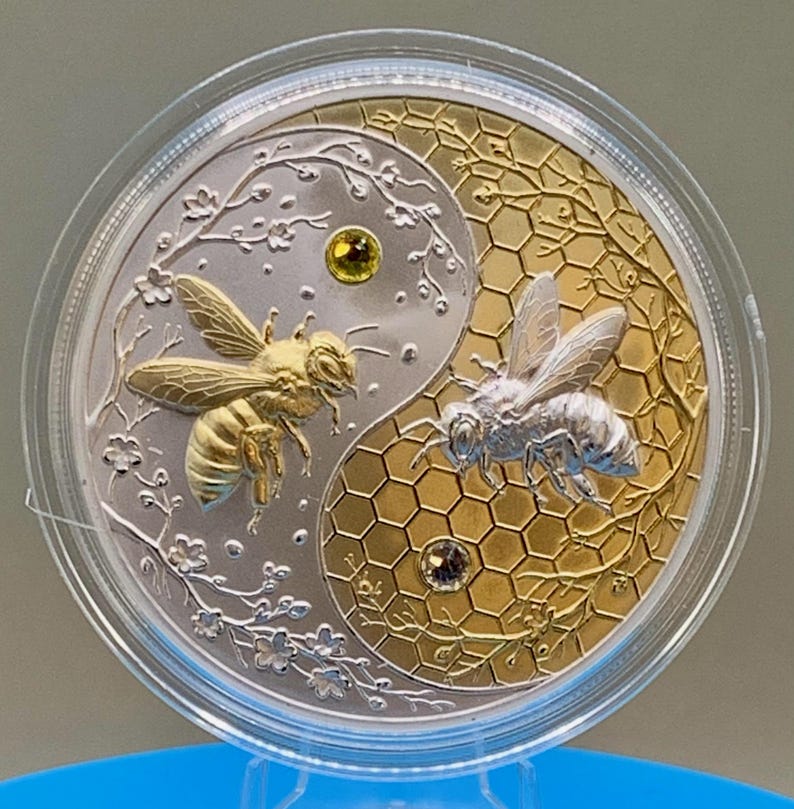 Straight-on view of the Harmony Bee copper round in its capsule, highlighting the raised gold and silver gilded yin-yang bee design and gemstone accents.