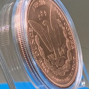 Angled view of the copper round's reverse side, showing the eagle-and-wreath "Copper Bullion Round" design in a protective capsule