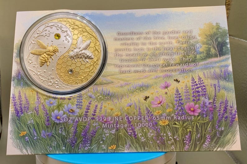 Harmony Bee copper round in its capsule laid on the printed certificate card, which features a wildflower meadow illustration and text reading 5OZ AVDP .999 FINE COPPER, 65mm Radius, Mintage: 10000.