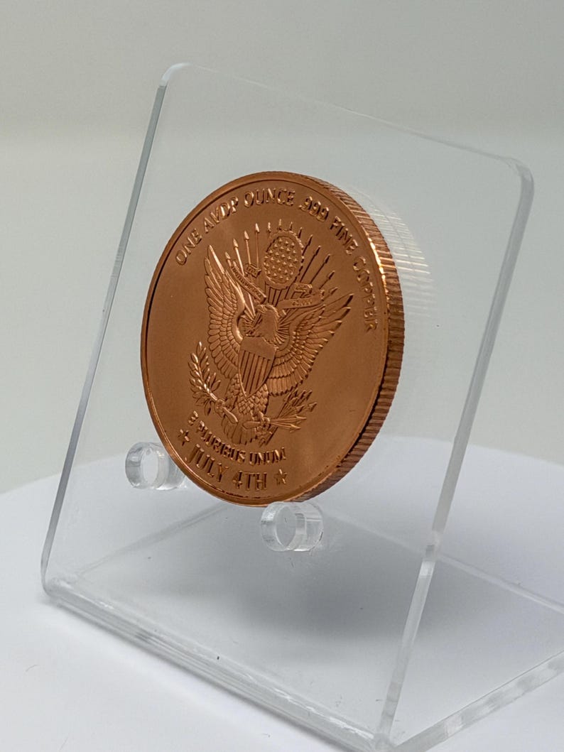 Angled rear view of the 1 oz copper round showing the Great Seal eagle reverse, tilted on a clear acrylic stand
